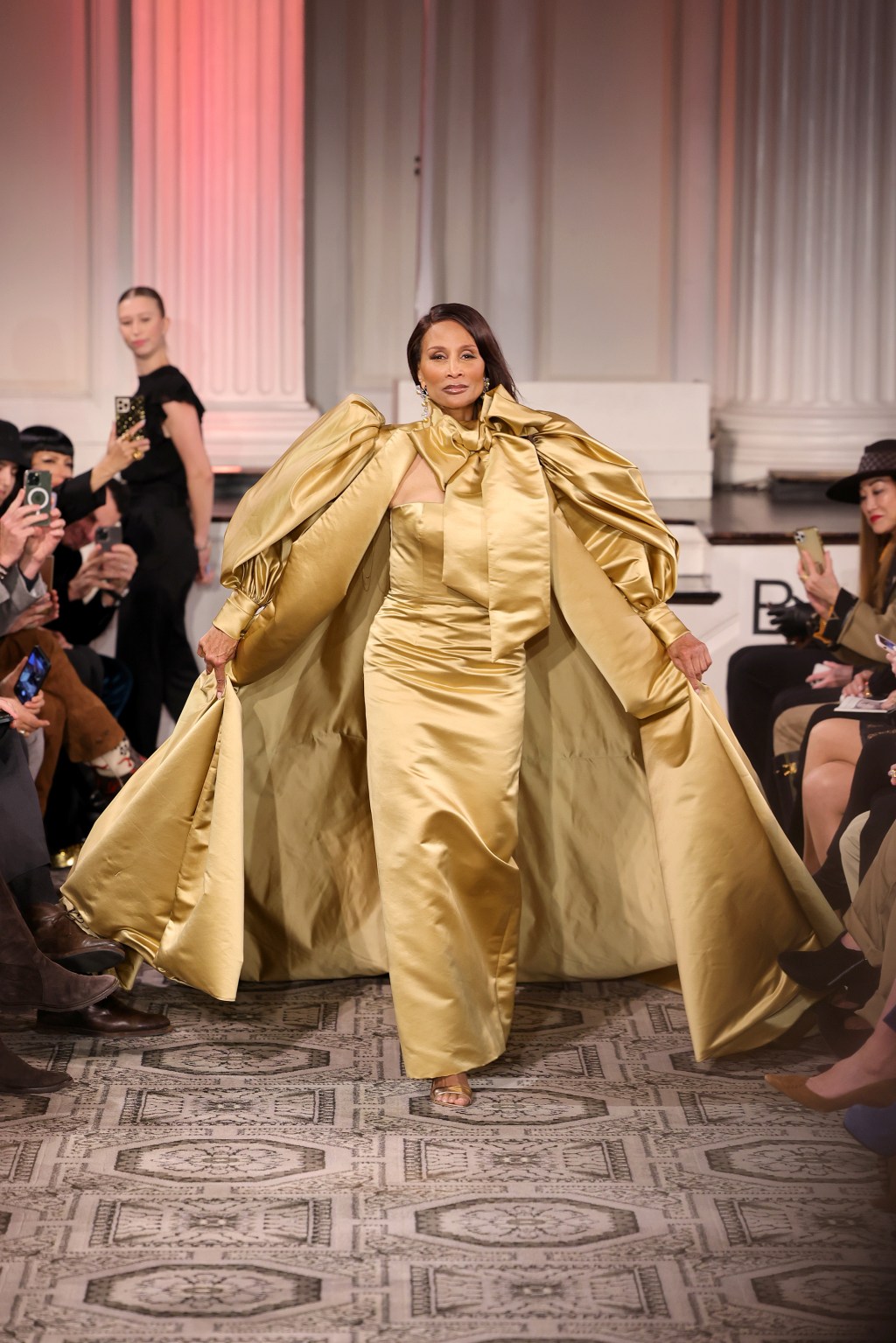 Beverly Johnson on runway in gold dress.