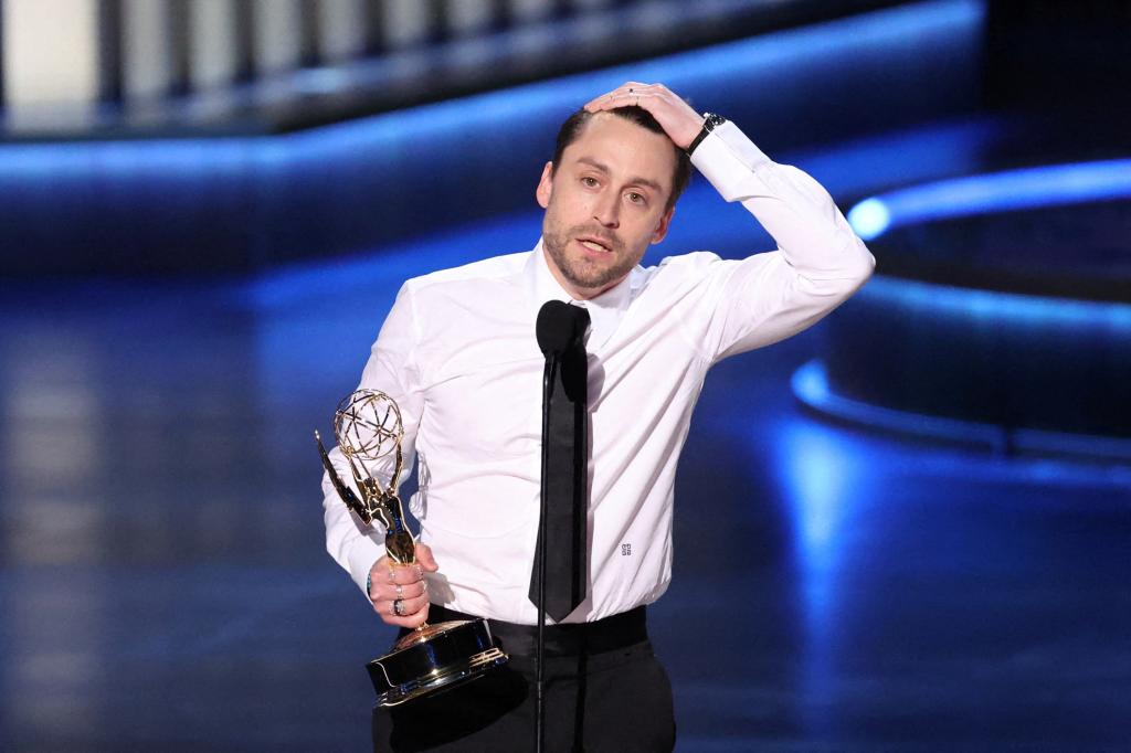 Kieran Culkin onstage at the Emmys, with one hand on his head and the other holding the award