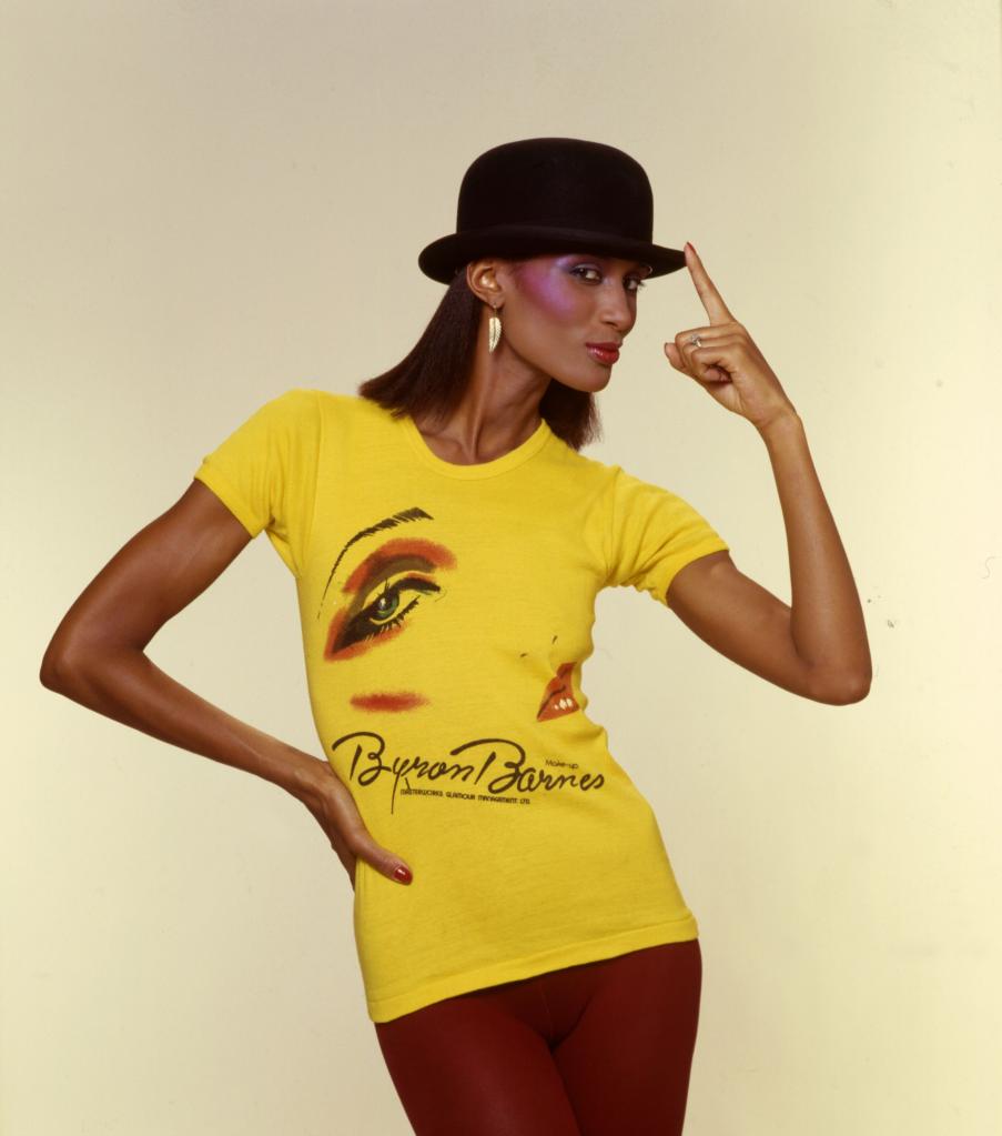 Beverly Johnson modeling in yellow shirt and black top hat.